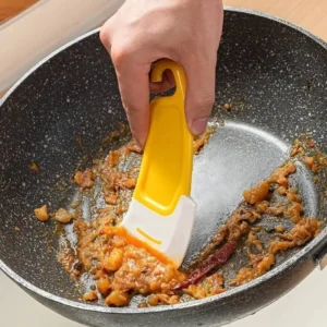 Silicone scraper cleaning stuck food residue from non-stick frying pan without scratching